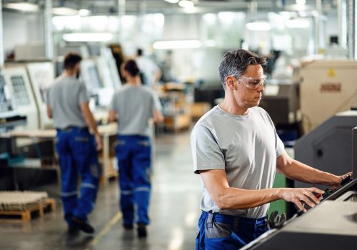 Mid adult worker operating a CNC machine while working in industrial facility.